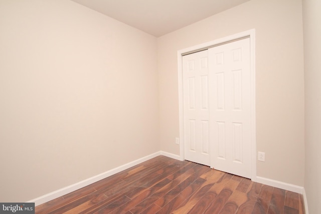 unfurnished bedroom featuring dark wood finished floors, baseboards, and a closet