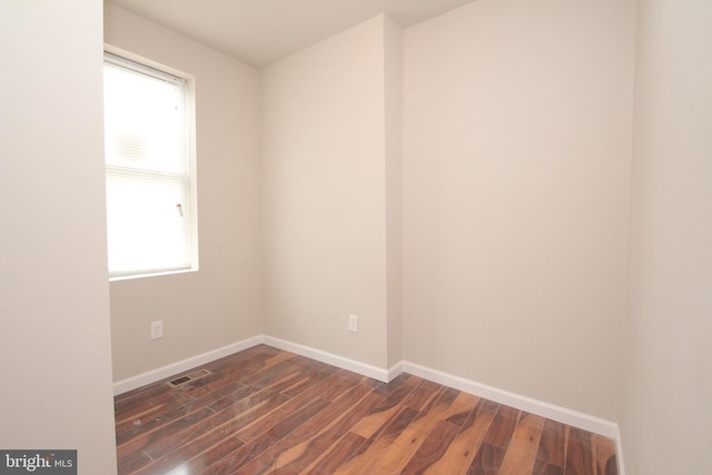 empty room featuring visible vents, baseboards, and dark wood finished floors