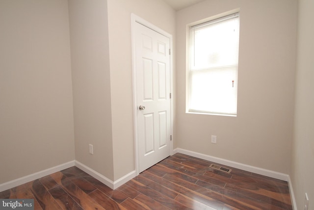 spare room with dark wood finished floors, visible vents, and baseboards