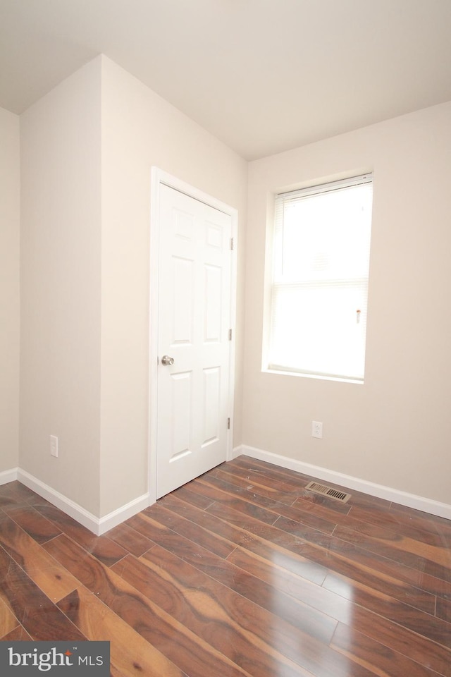 spare room with wood finished floors, visible vents, and baseboards