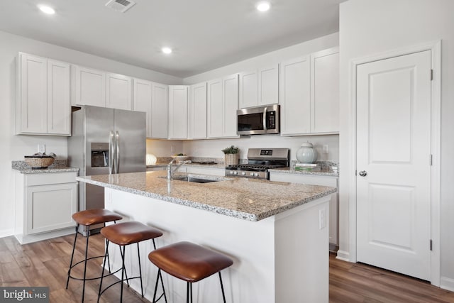 kitchen with a sink, stainless steel appliances, wood finished floors, and a kitchen breakfast bar