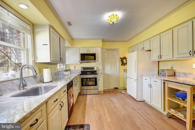 kitchen featuring light stone counters, stainless steel appliances, a sink, visible vents, and light wood-style floors