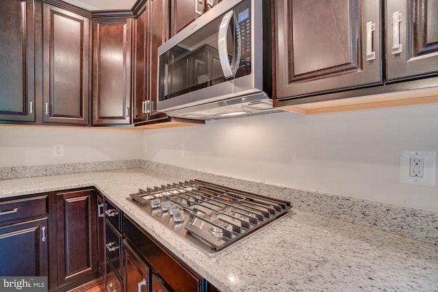 kitchen with light stone countertops, dark brown cabinets, and appliances with stainless steel finishes