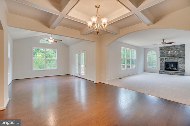 unfurnished living room featuring ceiling fan with notable chandelier, arched walkways, beamed ceiling, a fireplace, and wood finished floors