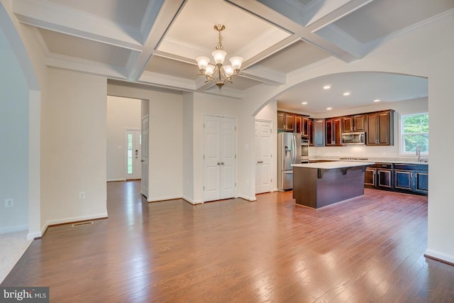 kitchen featuring a breakfast bar area, dark wood finished floors, stainless steel appliances, arched walkways, and an inviting chandelier
