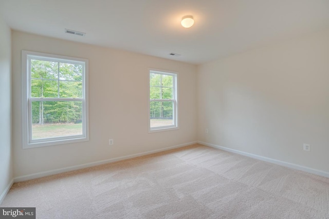 spare room with baseboards, light colored carpet, and visible vents