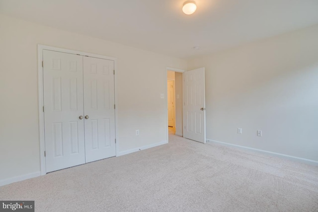 unfurnished bedroom featuring light colored carpet, a closet, and baseboards
