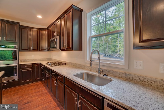 kitchen with a sink, wood finished floors, appliances with stainless steel finishes, and dark brown cabinets