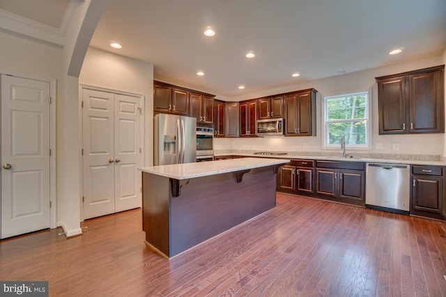 kitchen with dark brown cabinetry, a sink, a breakfast bar, dark wood-style floors, and stainless steel appliances