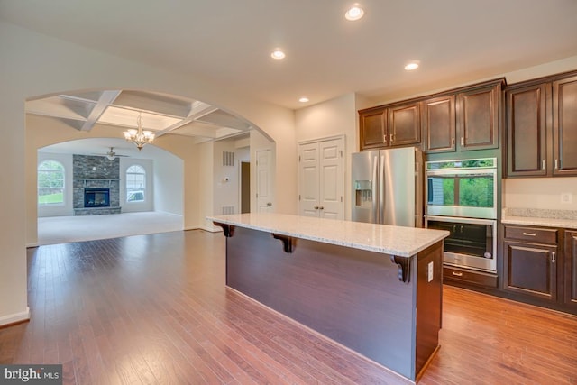 kitchen with coffered ceiling, a breakfast bar, light wood-type flooring, stainless steel appliances, and arched walkways