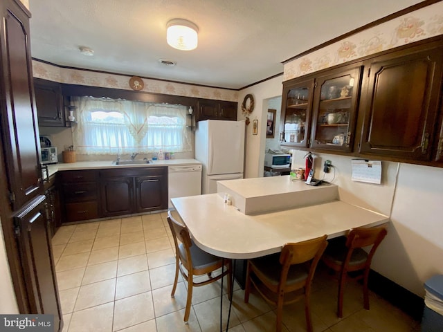 kitchen featuring white appliances, a sink, dark brown cabinets, light countertops, and wallpapered walls