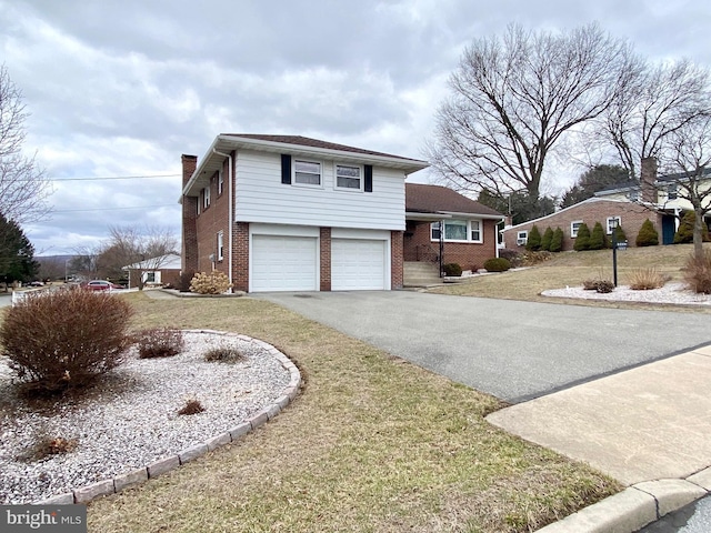 split level home with a garage, brick siding, driveway, a front lawn, and a chimney