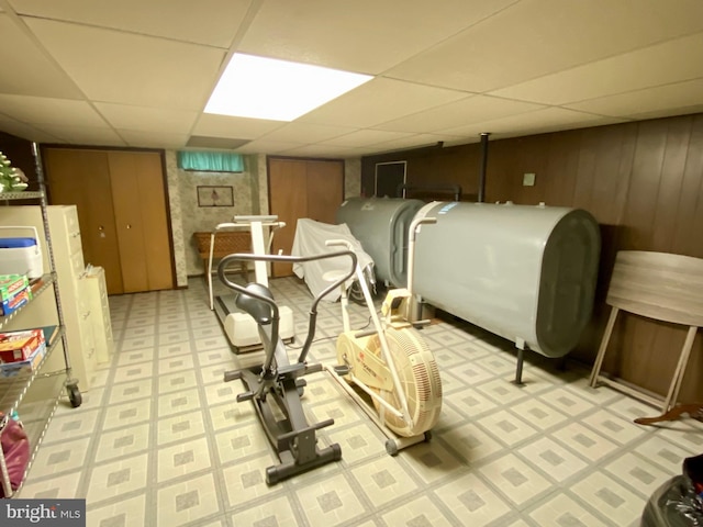 exercise area featuring a paneled ceiling, light floors, wood walls, and heating fuel