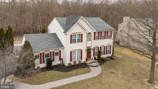 colonial-style house featuring entry steps, a front lawn, and roof with shingles