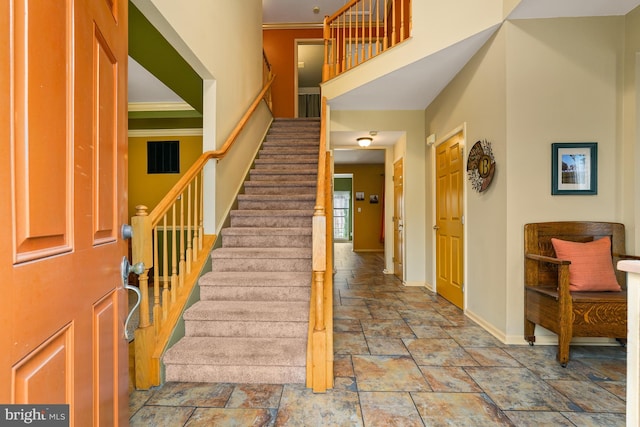 foyer with baseboards, stone finish flooring, a high ceiling, and crown molding