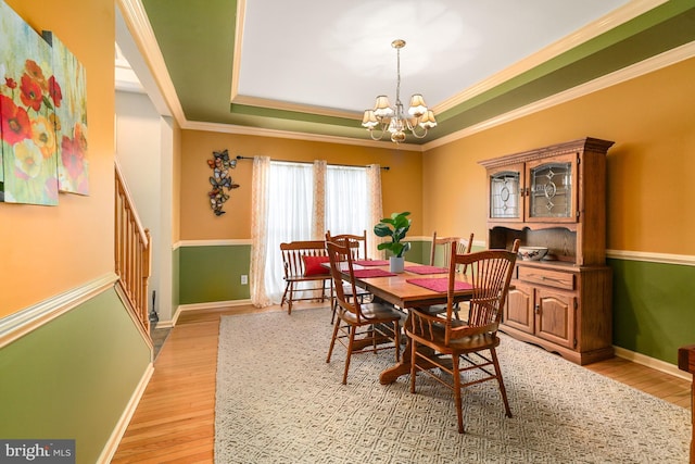 dining space featuring baseboards, light wood-type flooring, a raised ceiling, and an inviting chandelier