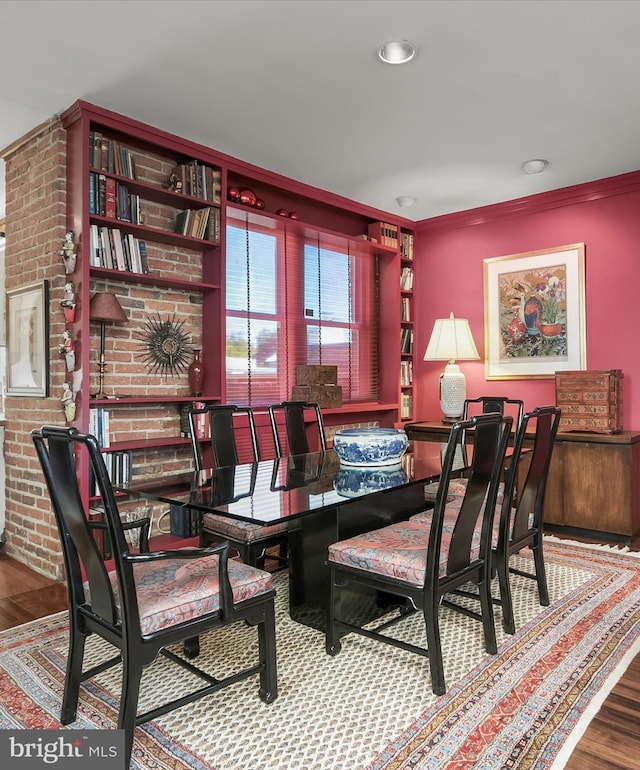 dining space with brick wall, ornamental molding, and wood finished floors