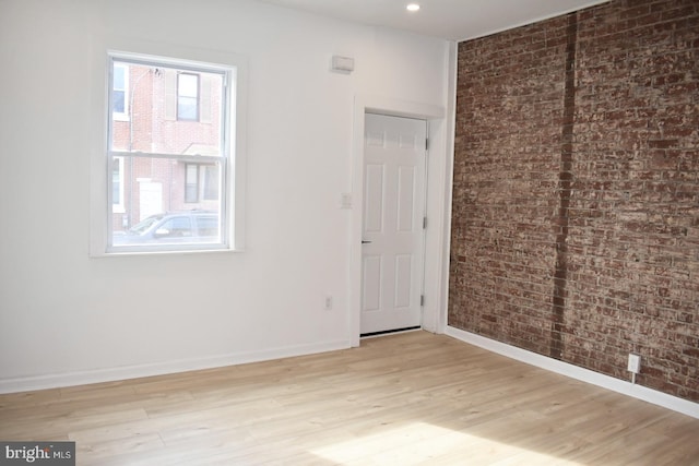 unfurnished bedroom with recessed lighting, light wood-style flooring, baseboards, and brick wall