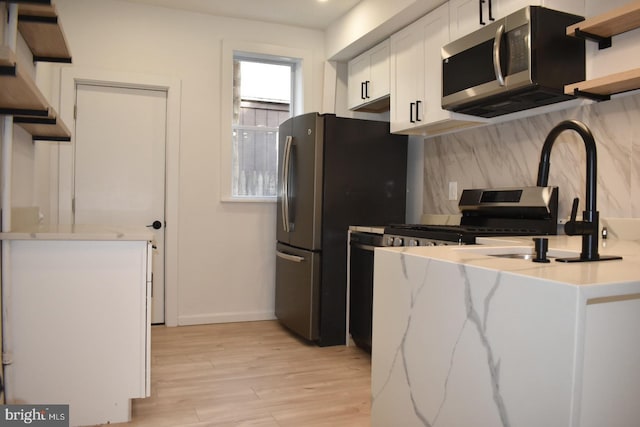 kitchen with light wood finished floors, decorative backsplash, stainless steel appliances, white cabinetry, and open shelves