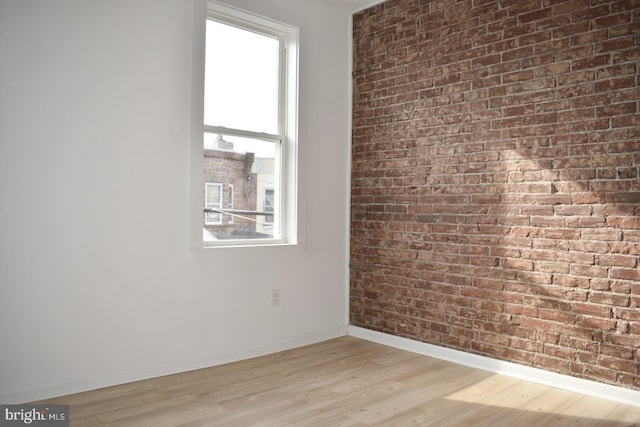 spare room with light wood-style floors, baseboards, and brick wall