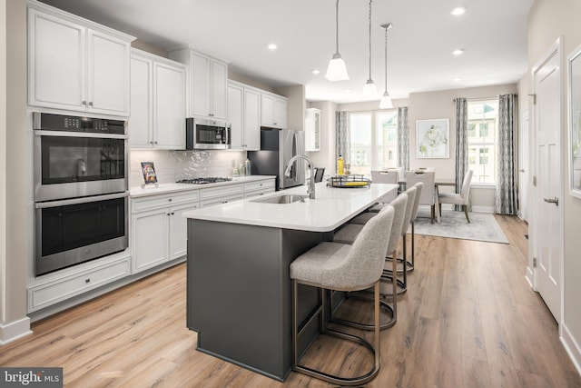 kitchen featuring a center island with sink, a sink, stainless steel appliances, light wood finished floors, and decorative backsplash