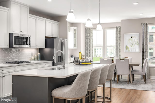 kitchen with light wood finished floors, tasteful backsplash, an island with sink, appliances with stainless steel finishes, and a sink