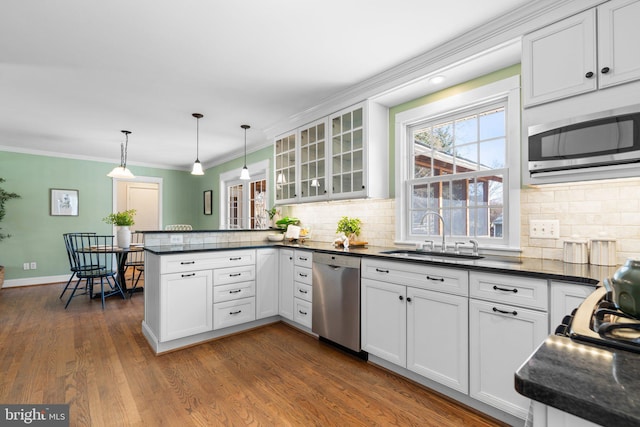 kitchen with a peninsula, dark wood-style flooring, a sink, stainless steel appliances, and dark countertops