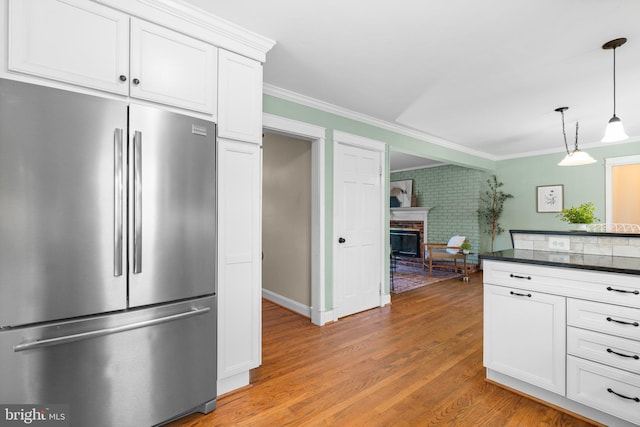 kitchen featuring ornamental molding, light wood-style flooring, a fireplace, stainless steel refrigerator, and white cabinetry