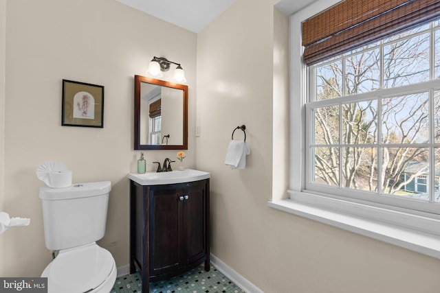 half bath featuring baseboards, plenty of natural light, toilet, and vanity