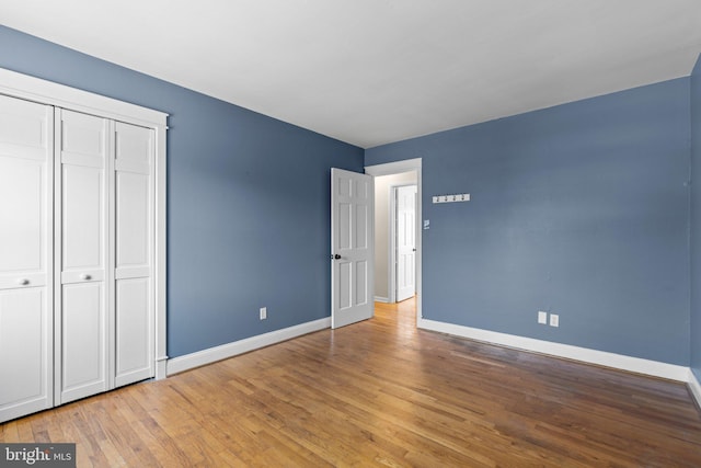 unfurnished bedroom featuring hardwood / wood-style flooring, baseboards, and a closet