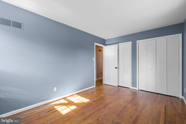 unfurnished bedroom featuring visible vents, baseboards, multiple closets, and hardwood / wood-style flooring