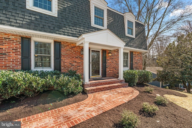 property entrance featuring mansard roof, brick siding, and a shingled roof