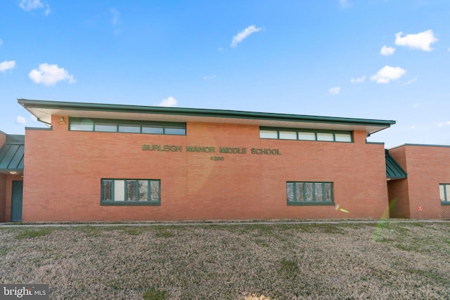 view of side of property featuring metal roof, brick siding, a lawn, and a standing seam roof