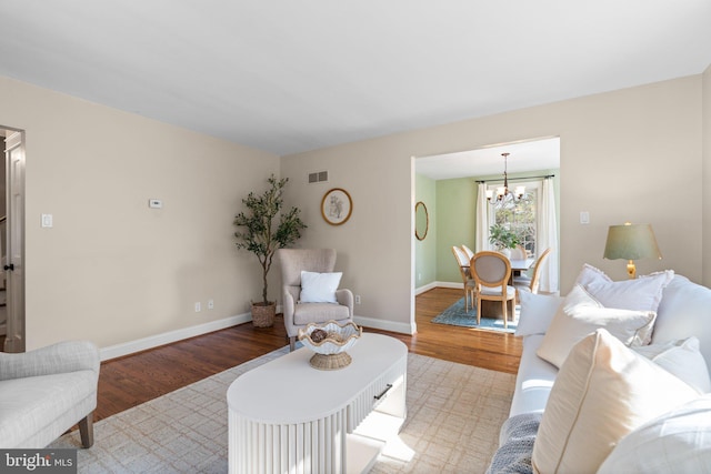 living area with a notable chandelier, visible vents, baseboards, and wood finished floors