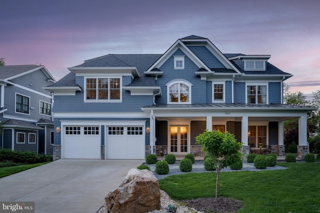 view of front of house featuring covered porch, a lawn, an attached garage, stone siding, and driveway