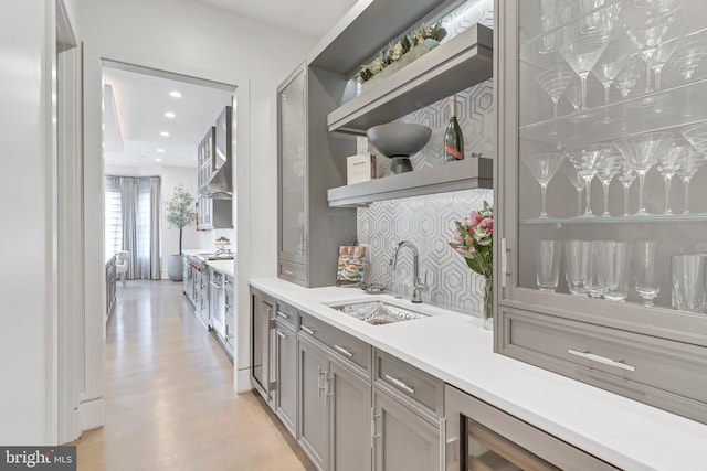 bar featuring light wood finished floors, tasteful backsplash, wall chimney range hood, a sink, and recessed lighting