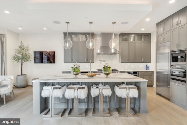 kitchen with tasteful backsplash, gray cabinets, built in refrigerator, and wall chimney exhaust hood