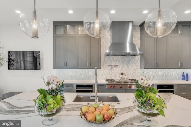 kitchen featuring oven, stainless steel gas stovetop, wall chimney range hood, and gray cabinetry