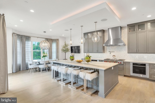 kitchen featuring wine cooler, a center island, gray cabinets, light wood-style floors, and wall chimney range hood