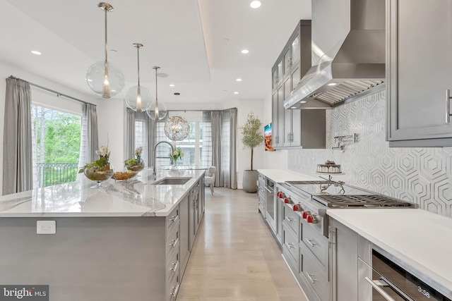 kitchen featuring a sink, appliances with stainless steel finishes, a large island, gray cabinets, and wall chimney exhaust hood