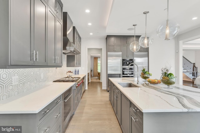 kitchen featuring tasteful backsplash, appliances with stainless steel finishes, gray cabinets, wall chimney range hood, and a sink