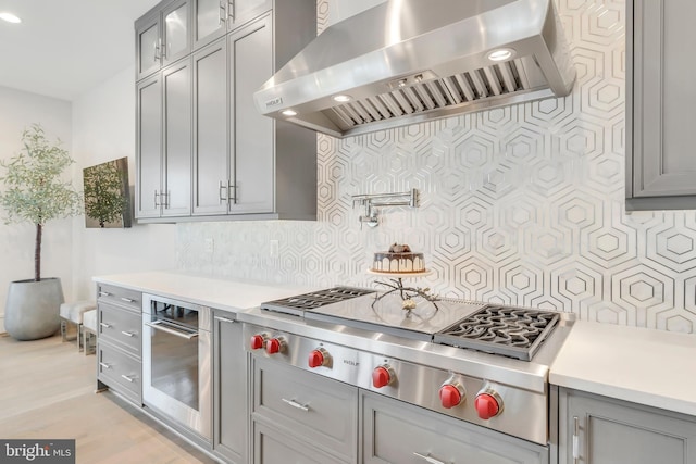 kitchen with wall chimney range hood, tasteful backsplash, gray cabinets, and light countertops