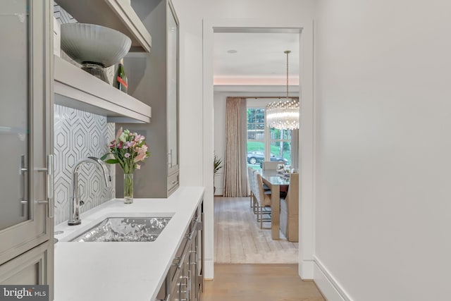 bar with a notable chandelier, a sink, light wood-style flooring, and baseboards