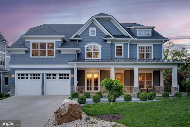 view of front facade featuring a porch, stone siding, french doors, concrete driveway, and a standing seam roof