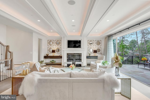 living room with recessed lighting, stairs, a raised ceiling, and a glass covered fireplace