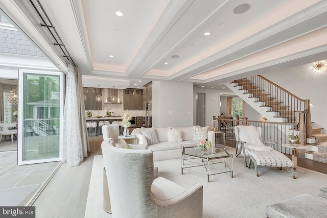 living room featuring light wood finished floors, a tray ceiling, stairway, and recessed lighting