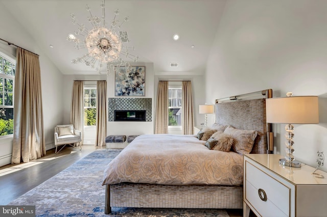 bedroom with visible vents, a tile fireplace, wood finished floors, high vaulted ceiling, and a notable chandelier