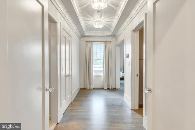 hall featuring a notable chandelier, a raised ceiling, crown molding, and wood finished floors