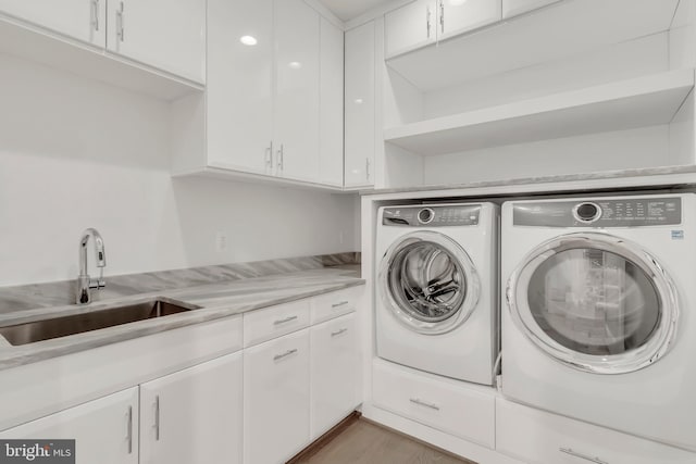 laundry room with washing machine and dryer, cabinet space, a sink, and wood finished floors