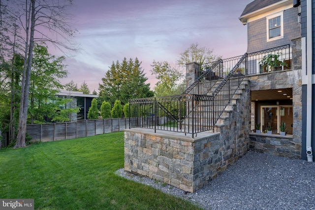 yard at dusk featuring fence and stairs